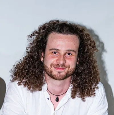 Maciej Czerniak, smiling, with long curly hair and a white shirt.