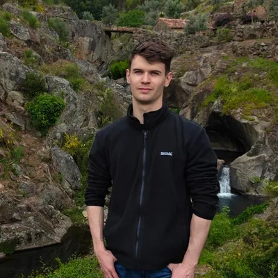 Szymon Chirowski, in a black fleece jacket, standing outdoors by a rocky stream.
